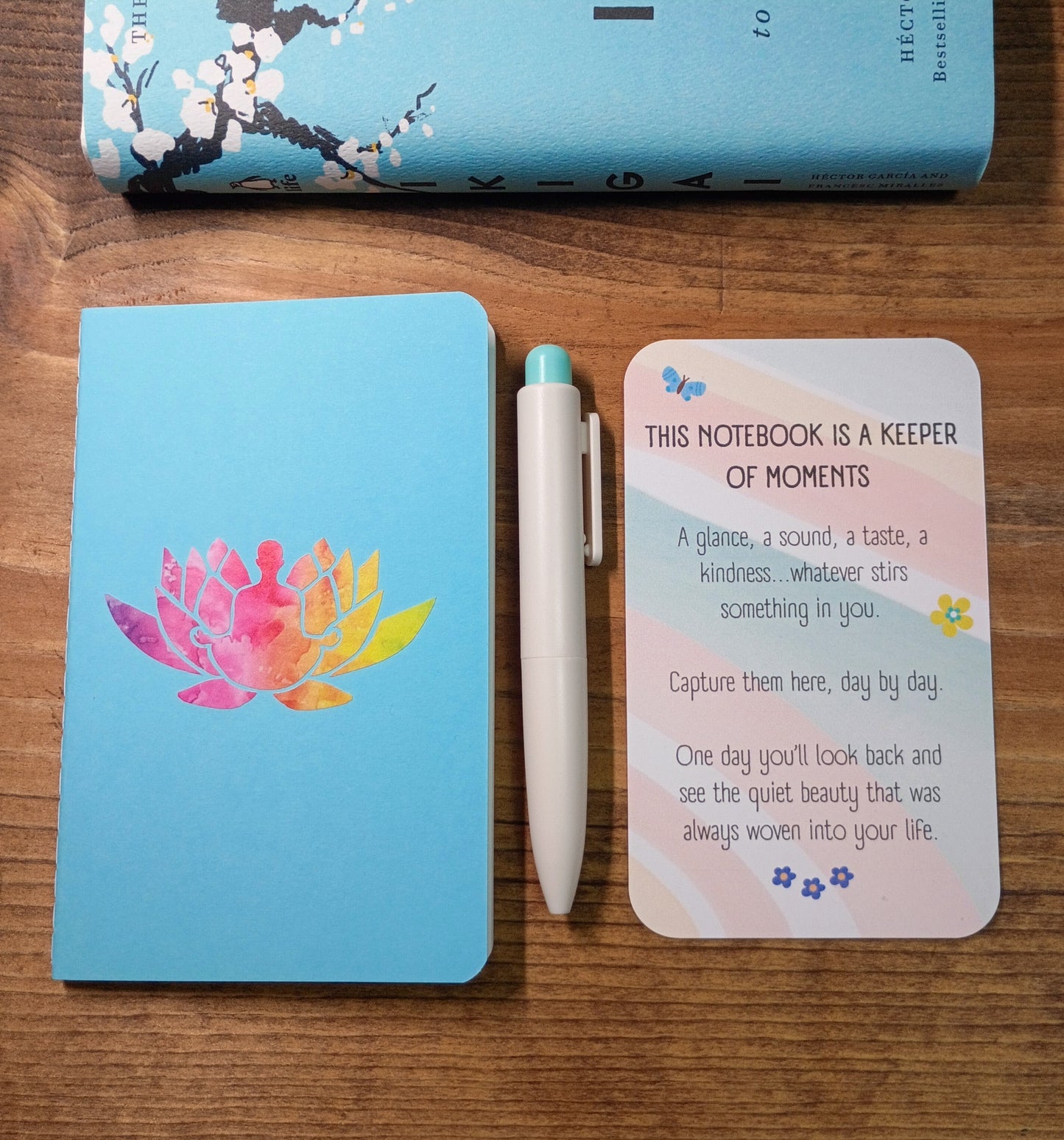 Notebook with lotus meditation design, pen, and inspirational card on a wooden surface