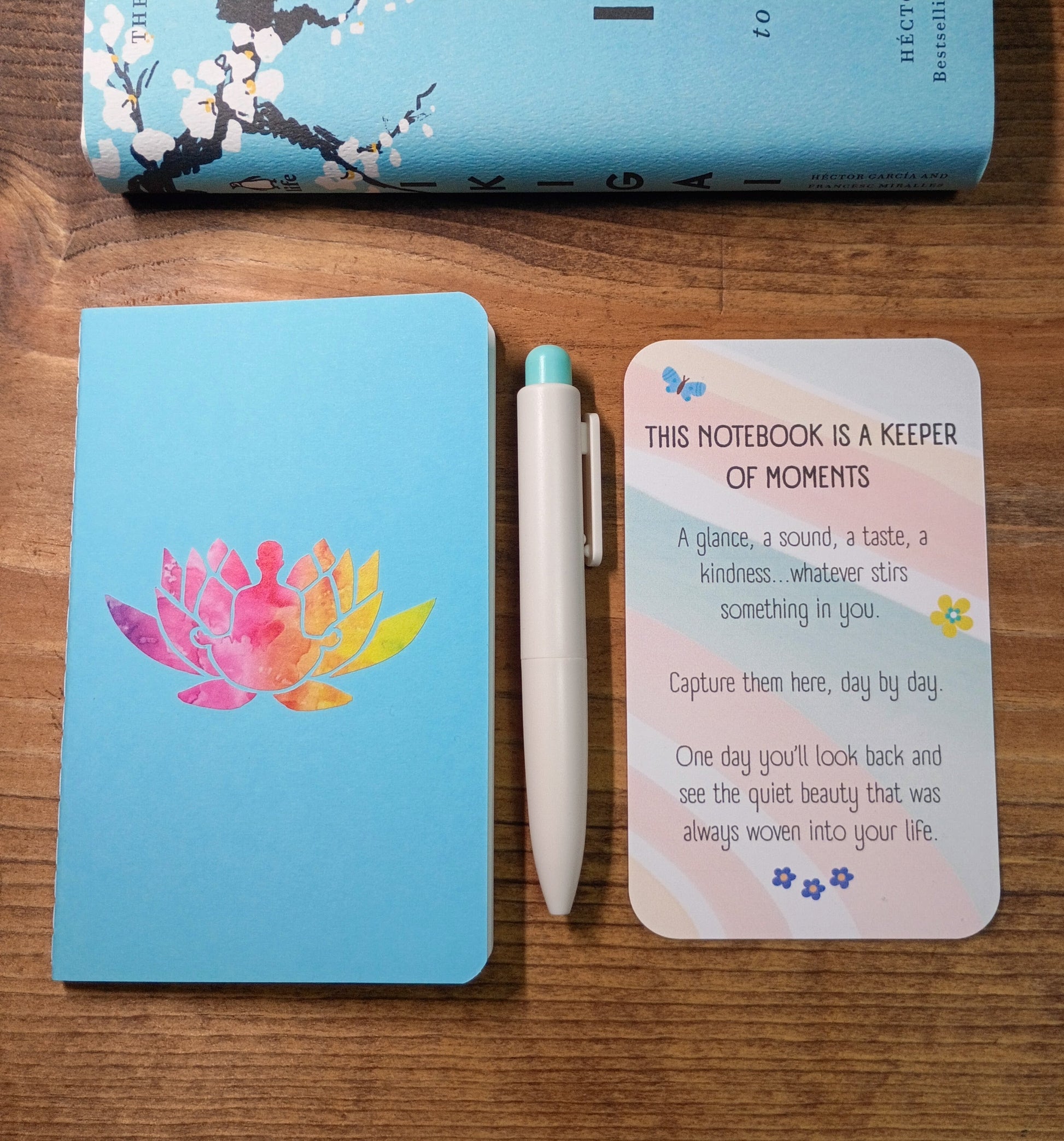 Notebook with lotus meditation design, pen, and inspirational card on a wooden surface